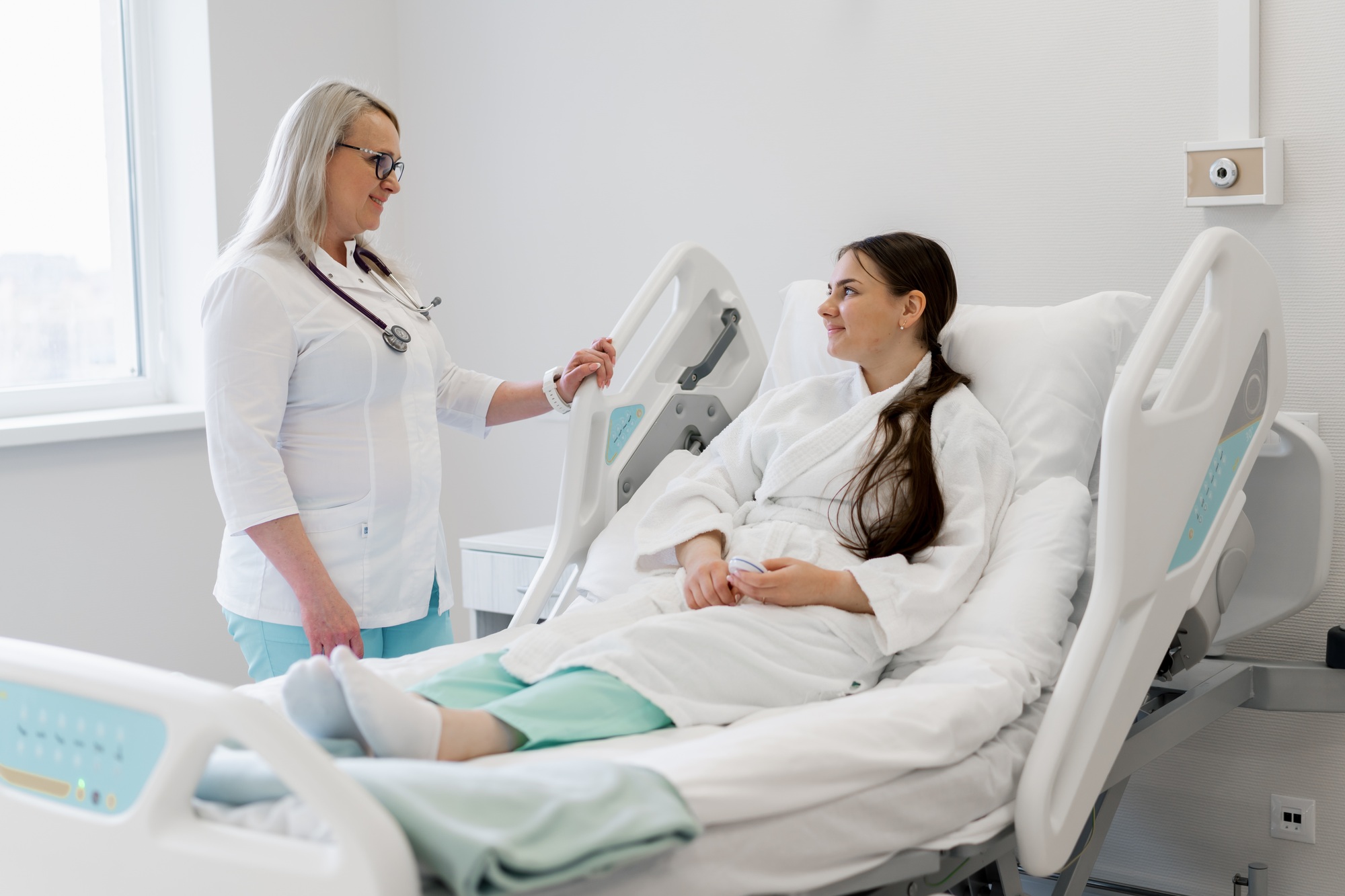 doctor standing by the bed in a hospital room and discussing a treatment plan with young patient