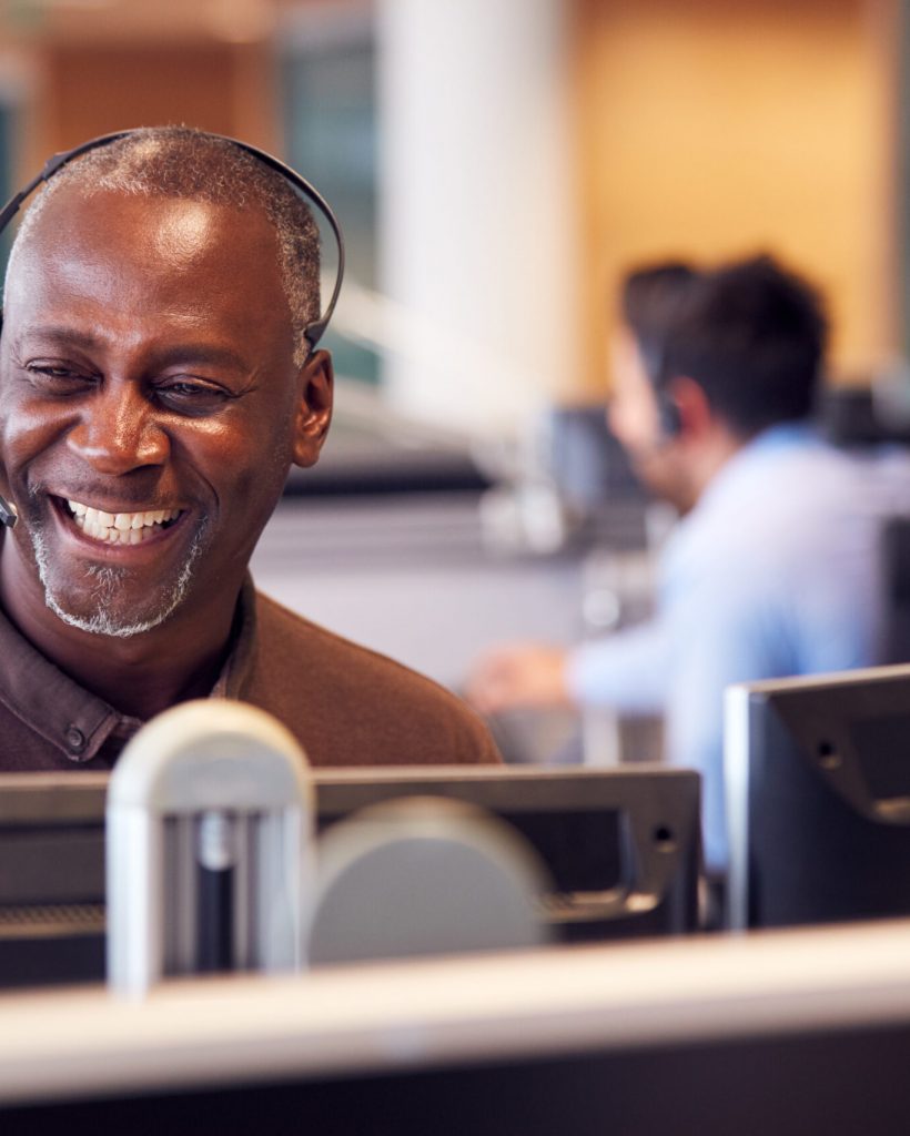 Mature Businessman Wearing Telephone Headset Talking To Caller In Customer Services Department