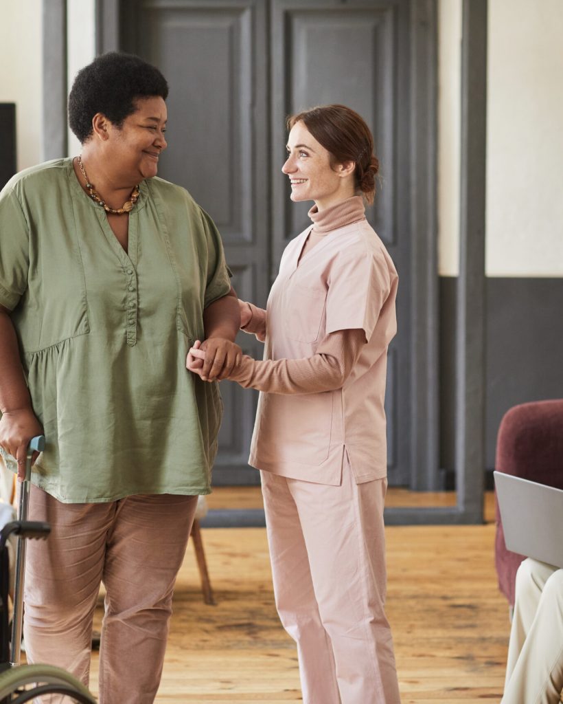 Portrait of smiling young woman helping seniors in modern retirement home, copy space